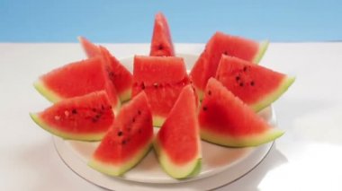 Sulu olgun karpuz mavi arka planda beyaz bir tabakta parçalara bölünmüş bir daire şeklinde döner.