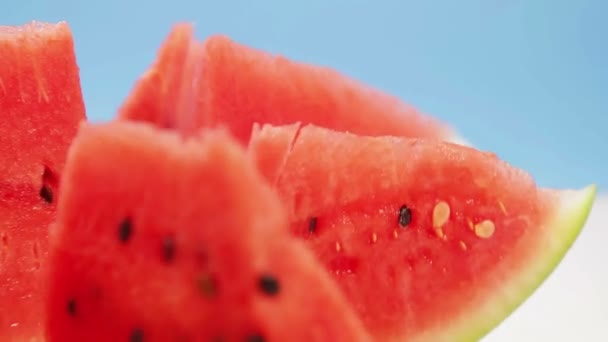 Des morceaux de pastèque rouge juteuse coupés sur un fond bleu tournent en cercle. — Video