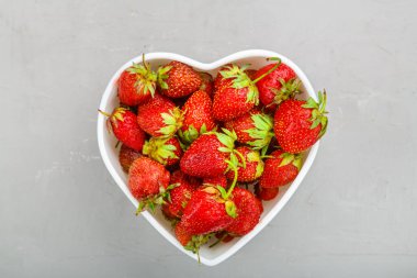 Gri arka planda kalp şeklinde bir tabakta taze çilekler. Yatay fotoğraf
