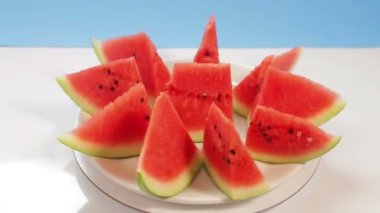 Sulu olgun karpuz mavi arka planda beyaz bir tabakta parçalara bölünmüş bir daire şeklinde döner.