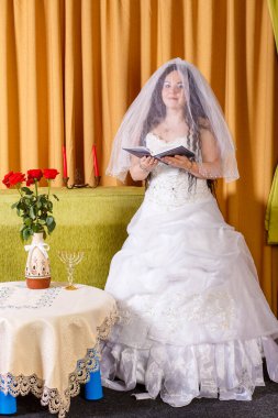 Beyaz elbiseli Yahudi gelin, çiçekli bir masada yüzü örtülü hupa töreninden önce dua okuyor..