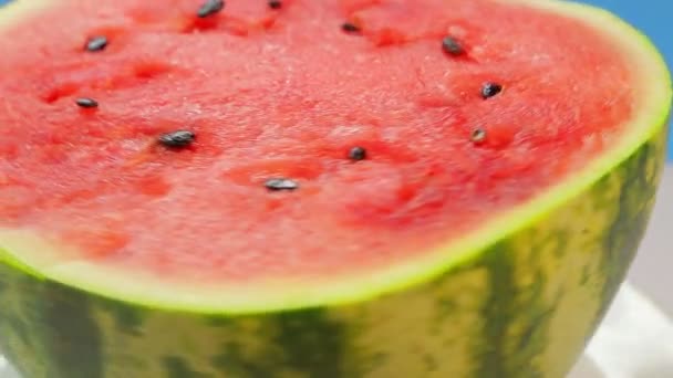 Die Hälfte einer reifen, saftigen Wassermelone auf einem Teller auf blauem Hintergrund dreht sich im Kreis — Stockvideo