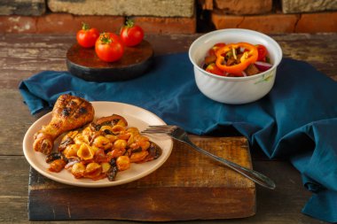 Domatesli deniz kabuğu makarnası, tavuk budu, ızgarada pişmiş, mavi peçete, çatal ve sebze salatasının yanında. Yatay fotoğraf