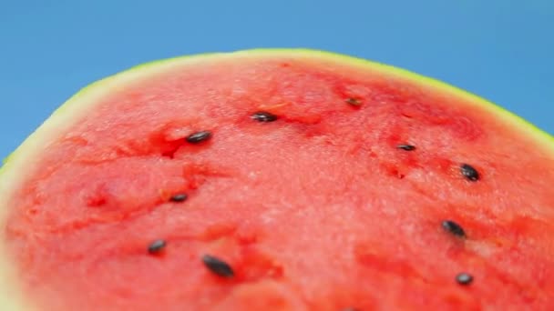 Hälften av en mogen saftig vattenmelon på en blå bakgrund rotera i en cirkel — Stockvideo