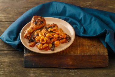 Domatesli deniz kabuğu makarnası ve mavi peçetede ızgara tavuk bacağı. Yatay fotoğraf