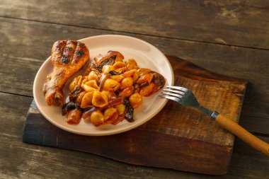 Domatesli deniz kabuğu makarnası ve bir çatalın yanındaki ahşap tezgahta ızgara tavuk budu. Yatay fotoğraf