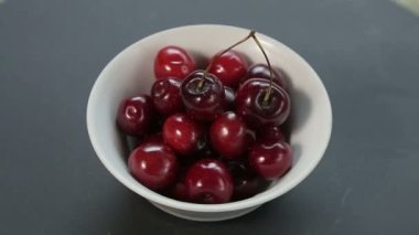 Olgun sulu kirazlar beyaz bir kase içinde daire şeklinde döner..