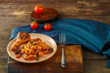 Domatesli deniz kabuğu makarnası, ızgarada pişmiş tavuk budu ve domateslerin yanında peçete..