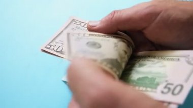 Erkek eller mavi bir arka planda dolar sayıyor.