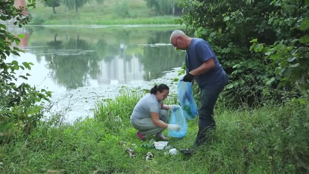 Un uomo e una donna volontari in un parco vicino all'acqua raccolgono rifiuti di plastica — Video Stock