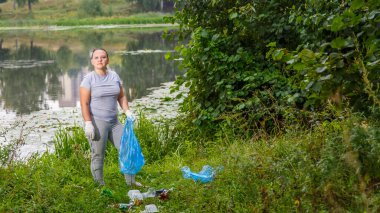 Bir kadın gönüllü parktaki çöpleri temizliyor. Yatay fotoğraf
