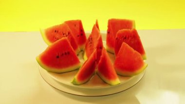 Sulu kırmızı karpuz parçaları beyaz bir tabakta sarı bir zemin üzerinde daire şeklinde döner.