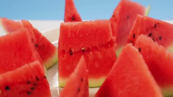 Bitar av mogen saftig vattenmelon på en platta på en blå bakgrund rotera i en cirkel — Stockvideo