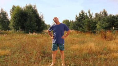 Orta yaşlı bir adam sabah çayırda jimnastik yapıyor.