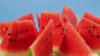 Olgun karpuz parçaları mavi arka planda bir tabakta daire şeklinde döner.