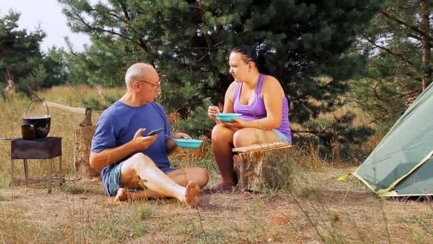 テントの近くの男と女が自然の中で食べ、男は食事をしながらも、 1分間ガジェットなしで行くことはできません。 — ストック動画