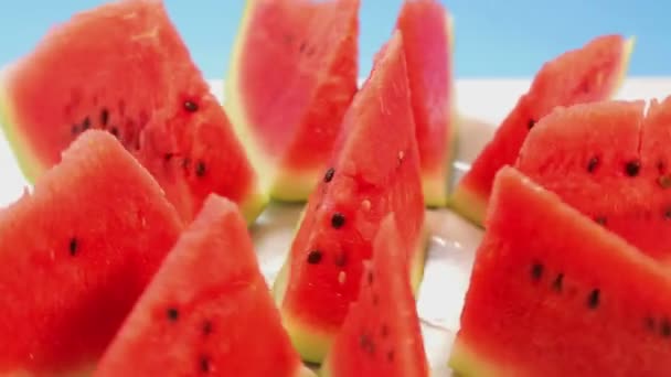 Bitar av mogen vattenmelon på en platta på en blå bakgrund rotera i en cirkel. — Stockvideo