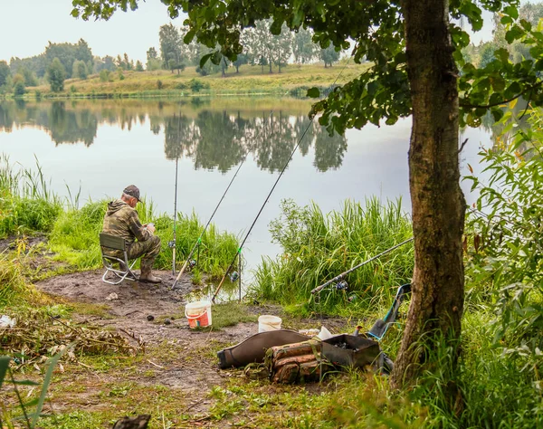 Un pescatore uomo con una canna da pesca sulla riva del fiume in una giornata di sole è la pesca. — Foto Stock