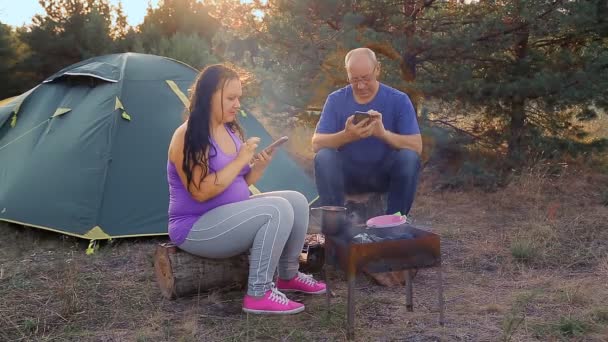 男と女はキャンプファイヤーのテントの近くでカップルと結婚したガジェットを再生 — ストック動画