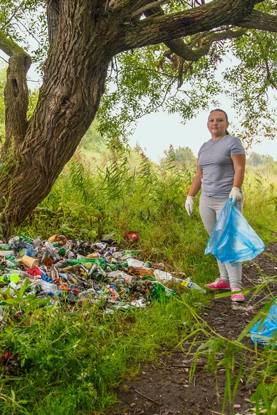 Young volunteer woman cleans up garbage at a landfill in the park.Young volunteer woman cleans up garbage at a landfill in the park. Vertical photo