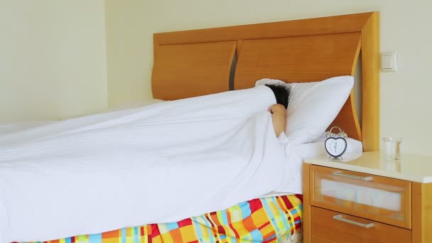 Egy nő az ágyban felébred egy ébresztőóra hangjából, kikapcsolja és újra elalszik, takaróval borítva. — Stock videók