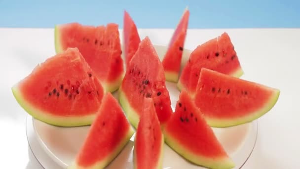 Lédús érett görögdinnye szeletek megállapított fehér lemez a kék háttér forog egy körben — Stock videók