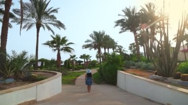 Mavi şapkalı ve üniformalı bir kadın Kızıl Deniz kıyısındaki hurma ağaçları arasında yürüyor. Arkadan ateş ediyorlar.