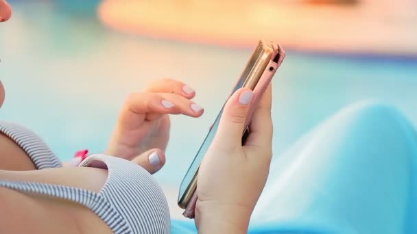 Les mains d'une femme en maillot de bain sur une chaise longue près de la piscine communiquent dans un smartphone — Video