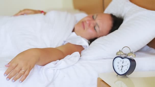 Uma mulher descontente acorda do som de um despertador, desliga-o e adormece novamente — Vídeo de Stock