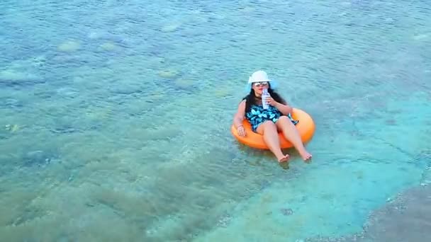 一个戴着蓝色帽子和太阳镜的黑发女人在海岸附近的海面上游来游去，遥望远方 — 图库视频影像
