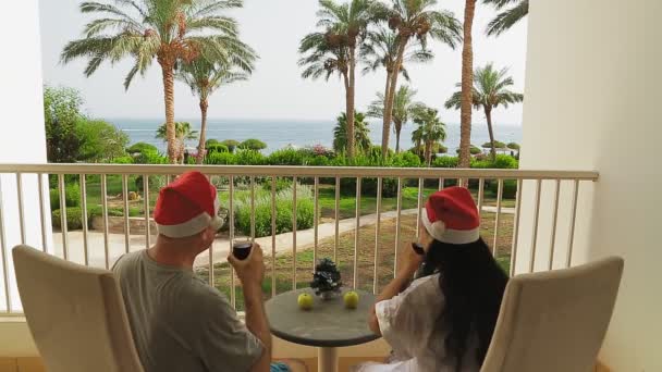 Een getrouwd stel viert Kerstmis en Nieuwjaar op het balkon met een kleine kerstboom op de tafel. — Stockvideo