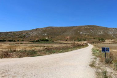 Temmuz 2024 'te Alto de Mostelares' e uzanan uzun toprak yol güneşli Meseta manzarası.