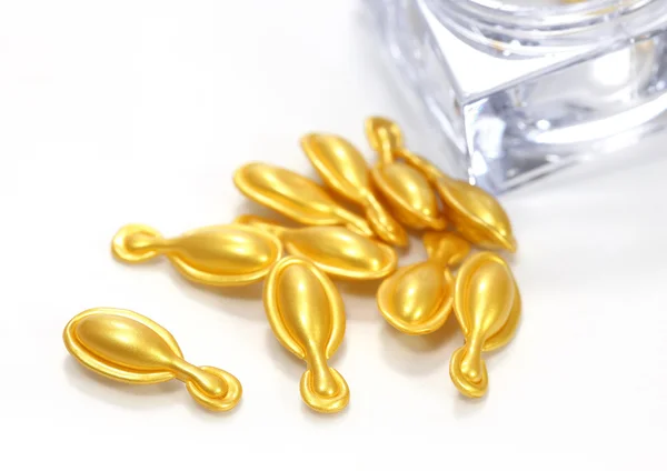 Gouden cosmetische capsules op witte achtergrond — Stockfoto