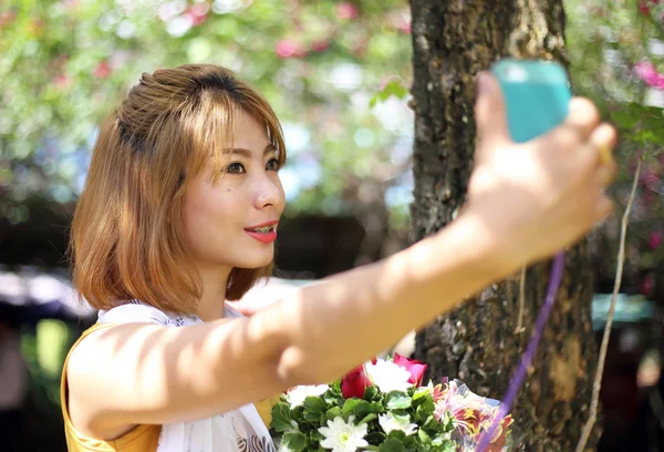 Asiatisk pige tager selfie foto hold blomst i haven - Stock-foto