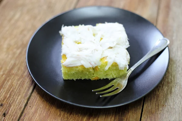 Pastel de coco en plato negro sobre mesa de madera — Foto de Stock