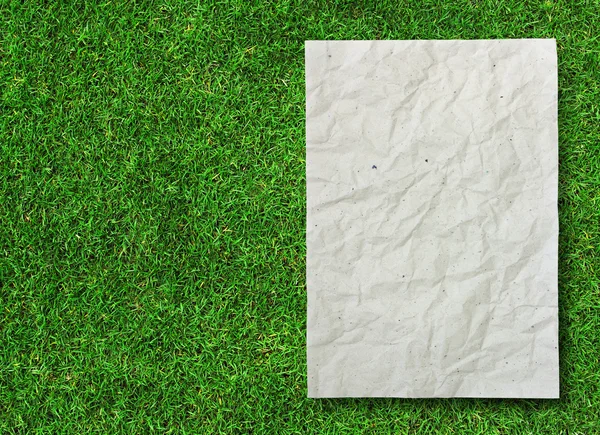 緑の草の背景にしわくちゃの再生紙 — ストック写真