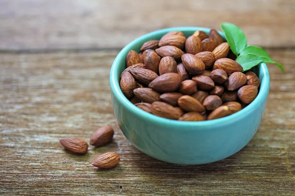 Almendras un tazón de cerámica sobre fondo de madera granulada — Foto de Stock