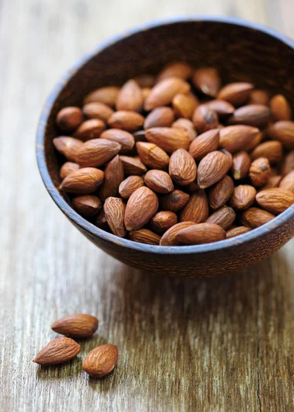 Almendras en tazón marrón sobre fondo de madera — Foto de Stock