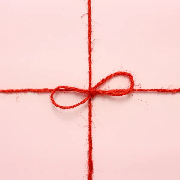 Red string bow on a pink paper background.