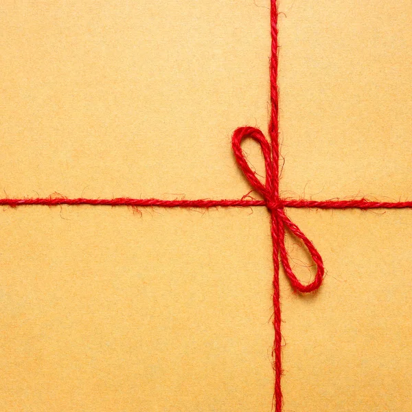 Stringa e pacchetto di carta marrone fiocco di stringa rosso contro involucro marrone — Foto Stock