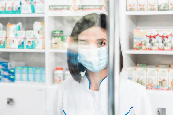 Retrato de um médico de grupo minoritário ou farmacêutico com máscara ao olhar através de um protetor protetor de tela — Fotografia de Stock