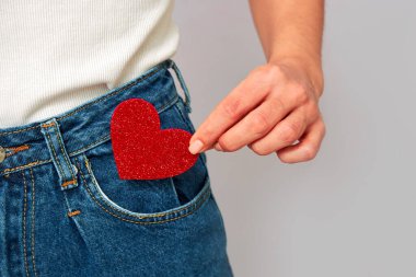 woman holding a small sparkling red heart putting it in or taking off the pocket of her jeans. Sharing and receiving Valentines, keeping love on you