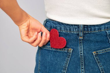 woman holding a small sparkling red heart putting it in or taking off the pocket of her jeans. Sharing and receiving Valentines, keeping love on you