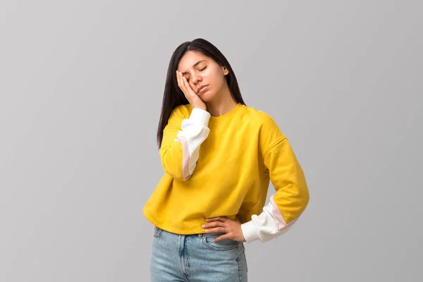 Tired young attractive multi ethnicity woman in trendy yellow sweater against light grey background with palm on her face — Stock fotografie