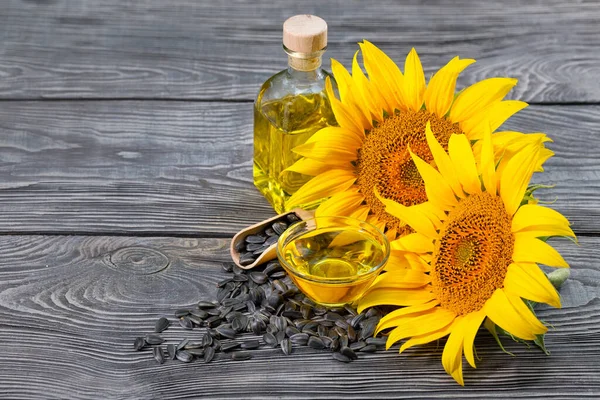 Flowers and sunflower seeds with oil in bottle and dish on table — Stock Photo, Image