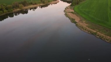 Pembe günbatımının yansımasıyla nehrin pürüzsüz sularında uçuyor yeşil arasında.