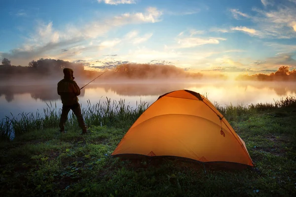 Fisherman near an orange tent on bank of misty river at sunset — Stock Photo, Image