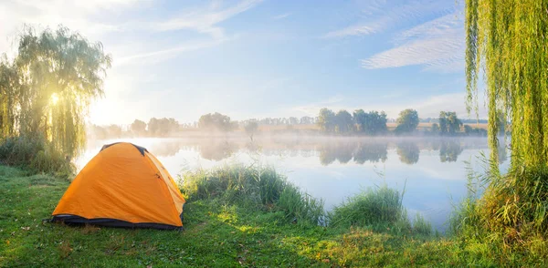 Praia do lago nebuloso com tenda laranja ao sol da manhã — Fotografia de Stock