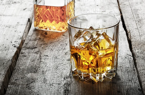 Faceted glass of whiskey with ice and a decanter — Stock Photo, Image
