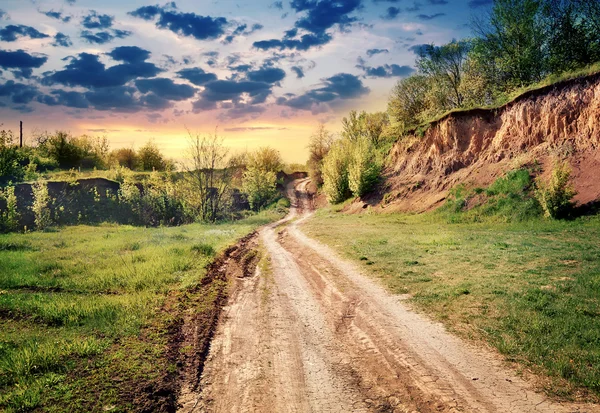 Dirt road passing by earthen cliff to the sun — Stock Photo, Image